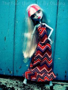 a doll with long blonde hair wearing a red and blue dress standing in front of a wooden door