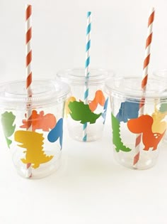 four plastic cups with different colored straws in them on a white surface, one is decorated with dinosaurs and the other has colorful striped paper straws