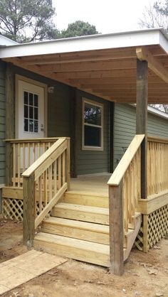 a small house with a covered porch and stairs leading to the front door, on a dirt lot