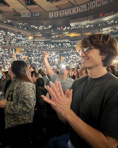 a man standing in front of a crowd holding his hands up to the sky with lights on them