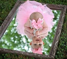 a baby girl is reflected in a mirror with her pink tutu and tiara