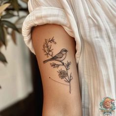 a small bird sitting on top of a branch next to a flower and leaves tattoo