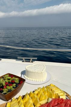 there is a cake and fruit on the table next to each other with water in the background