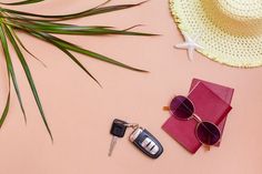 sunglasses, passport and keys on pink surface with palm leaf next to it in the foreground