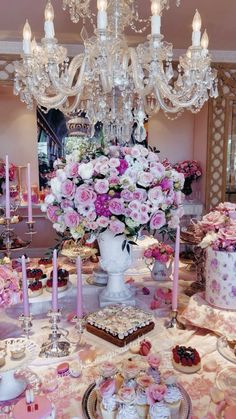 a table topped with cakes and cupcakes covered in frosting next to a chandelier