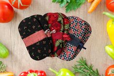 four oven mitts sitting on top of a wooden table surrounded by vegetables and herbs