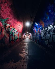 a dark tunnel with graffiti all over the walls and floor, along with a light at the end