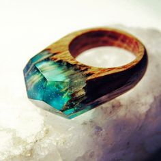 a wooden ring sitting on top of a rock covered in ice and snow with a blue green stone