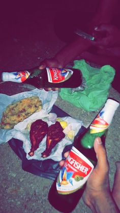 a person holding a bottle of beer next to some food on a table with other items