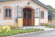 a small building with an open door and two windows on the front, surrounded by greenery