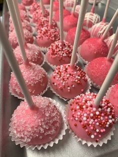 pink cake pops with white and red sprinkles are on display in a silver tray