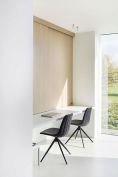 two black chairs sitting on top of a white table in front of a large window