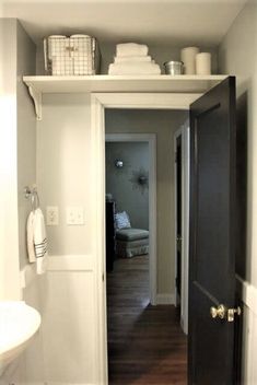 an open door leading to a bathroom with wood floors and white walls, in front of a sink