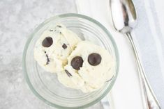 two ice creams with chocolate chips in a glass bowl next to a silver spoon