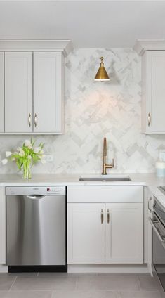 a white kitchen with stainless steel appliances and marble backsplash, gold faucet