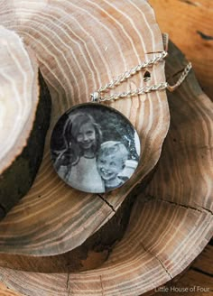 a necklace with a photo on it sitting on top of a piece of wood next to a tree