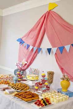 a table filled with lots of food on top of a white table covered in pink and blue flags