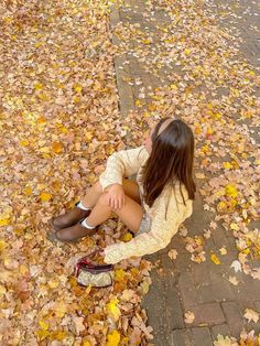 a woman sitting on the ground surrounded by leaves