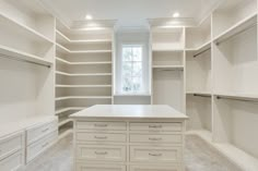 an empty walk in closet with white cabinets and drawers