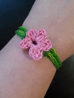 a pink crocheted flower bracelet on someone's wrist, with green leaves