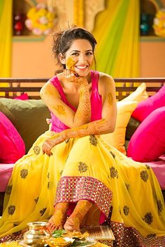 a woman sitting on top of a bed covered in yellow and pink colors holding her hands to her face