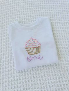 This hand embroidered T-shirt can be customized to your liking, with the name, nickname, or age of your toddler in the stitching font and color you prefer. This high quality, minimalistic design is perfect to slip on your toddler to celebrate their birthday! Hand Embroidered Toddler Shirt, Toddler Birthday Outfit, Cupcake Shirt, Bluey Party, T-shirt Broderie, Stitch Shirt, Baby Embroidery, Toddler Birthday, First Birthday Outfits