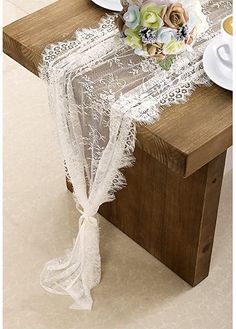 a table topped with plates and flowers on top of a wooden table covered in white lace