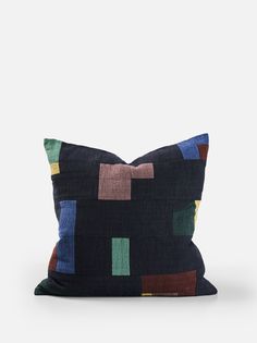 a black pillow with multicolored squares on the front and back, sitting on a white surface