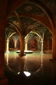 the interior of an old building with columns and arches, reflecting water in the floor