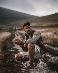 a man squatting down in the middle of a dirt road