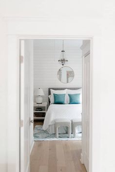 a white bed sitting in a bedroom next to a mirror on the wall and wooden floors