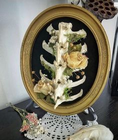 an ornate gold frame with dried flowers in it on a black table next to a white doily