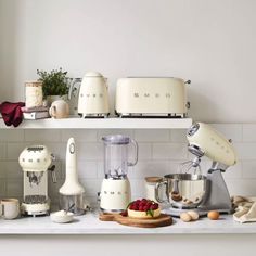 kitchen appliances are lined up on the shelf in front of the counter top, with one mixer and two blenders