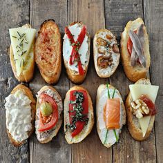 an assortment of breads with different types of toppings on them sitting on a wooden surface