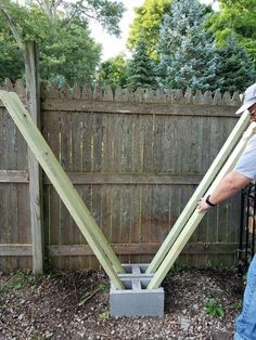 a man is holding two large pieces of wood in front of a fence