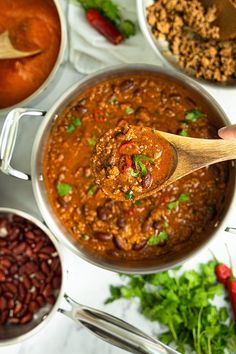 a wooden spoon in a pot filled with chili and beans next to other food items