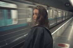 a woman standing in front of a train at a subway station with her eyes closed