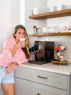 a woman is drinking from a coffee mug in the kitchen while standing next to her counter