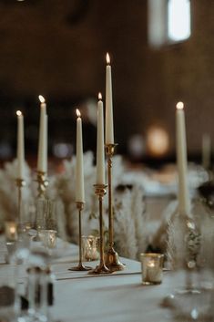 there are many candles on the table with white linens and place settings for guests to sit at