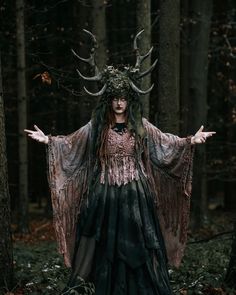 a woman dressed as a demon standing in the woods with her arms out and hands outstretched