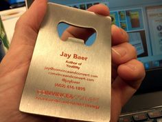 a person holding up a metal business card with a bottle opener on it's front