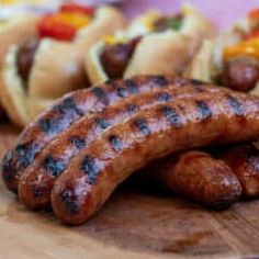 three hot dogs and two sausages on a cutting board next to other food items