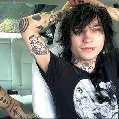 a man with black hair and tattoos sitting in the back seat of a car holding his head