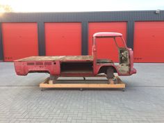 an old pick up truck is parked in front of red garage doors and a wooden pallet