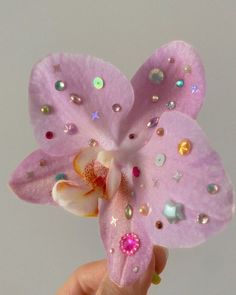 a hand holding a pink flower with lots of small jewels on it's petals