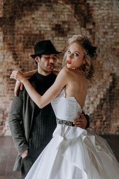 a man in a black hat is hugging a woman wearing a white wedding dress and jacket