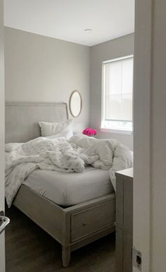 an unmade bed sitting in a bedroom next to a window with a round mirror on the wall