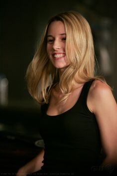 a woman with blonde hair smiling and looking at something in the distance while wearing a black tank top