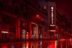 an empty city street at night with lights reflecting off the wet pavement and buildings in the background