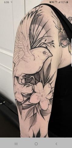 a woman's arm with a bird and flowers tattoo on her left side shoulder